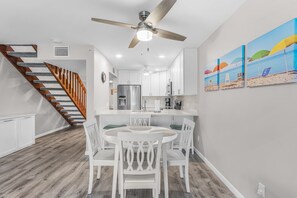 A modern kitchen with white cabinets, a stainless steel refrigerator, and a dining area with white chairs and a round table. - Coastal Bokeelia Getaway at Bocilla Island Club! (Bokeelia)