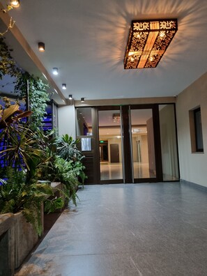 A hotel lobby with a modern design, featuring a glass door entrance, potted plants, and a ceiling light fixture. - Two-room apartment - Macrocentro Salta (Salta)