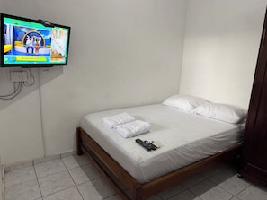 A hotel room with a bed, white linens, a TV mounted on the wall, and a remote control on the bed. - Rancho Pura Vida, San Blas Beach, La Libertad, Surf City, El Salvador (Playa San Blas)