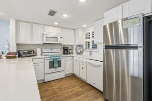 A modern kitchen with white cabinetry, stainless steel appliances, and a wooden floor. - Amelia South F1 - Hosted by Moore AI Rentals (Fernandina Beach)