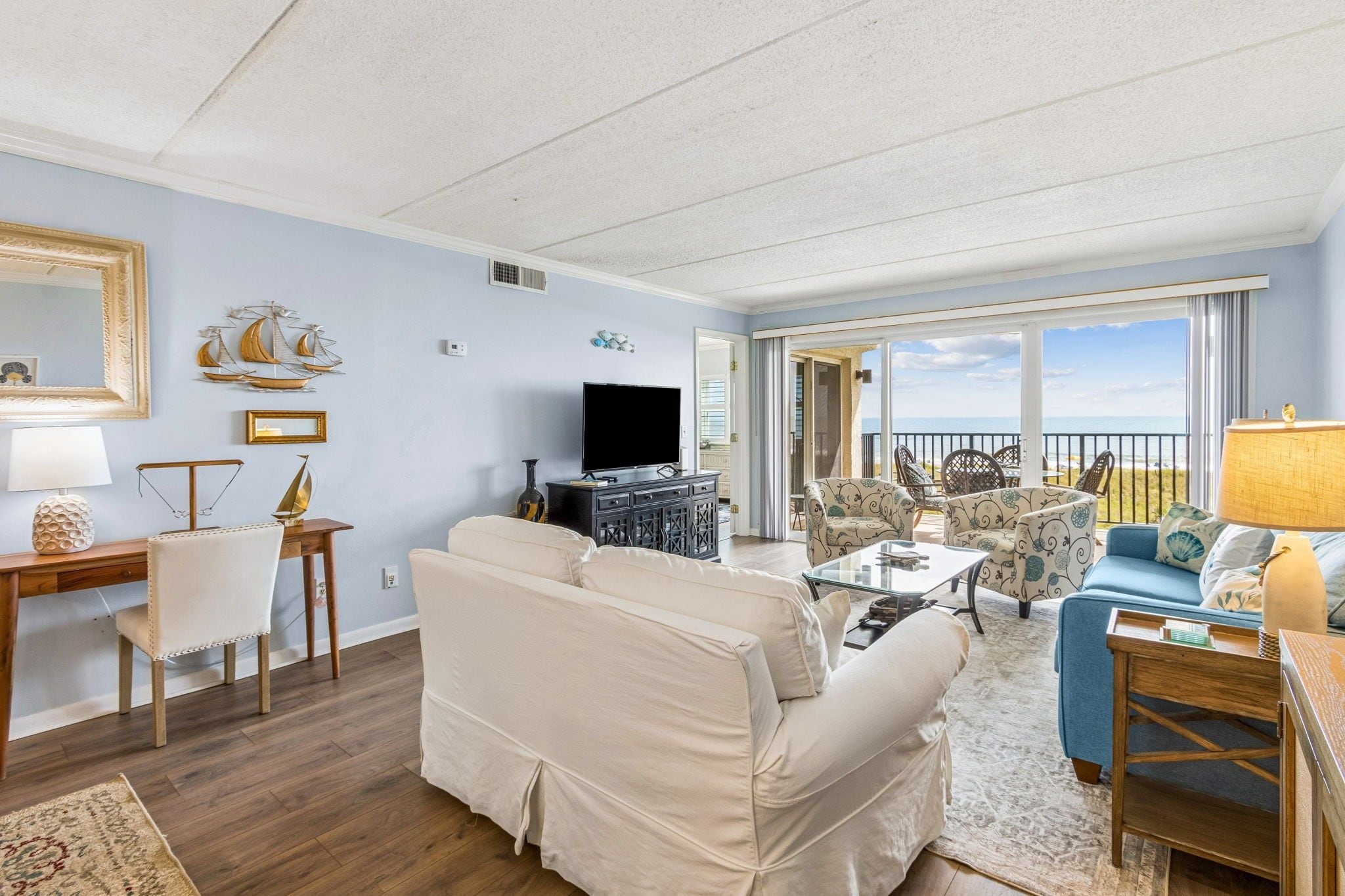 A living room with a sofa, chairs, a TV, and a balcony with a view.
