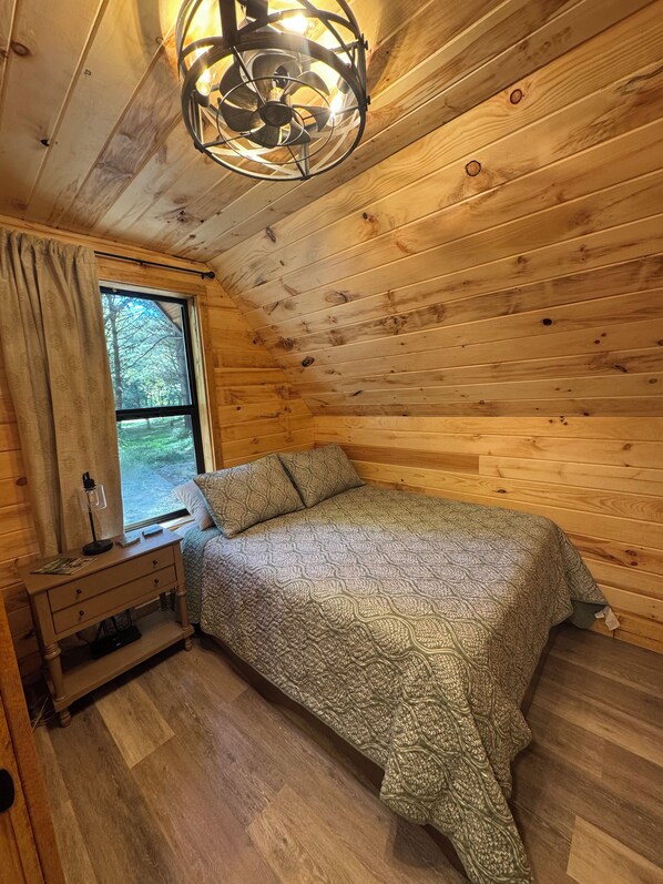 Une chambre dans un chalet en bois, avec un lit, une table de chevet, une lampe et une fenêtre.
