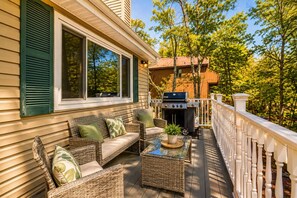 A covered outdoor seating area with wicker furniture and a grill. - Aurora Pines, a cozy Poconos retreat. (Tobyhanna)