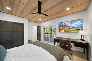 Ein Schlafzimmer mit Bett, Schreibtisch und Stuhl. An der Wand hängt ein Gemälde und es gibt einen Deckenventilator.