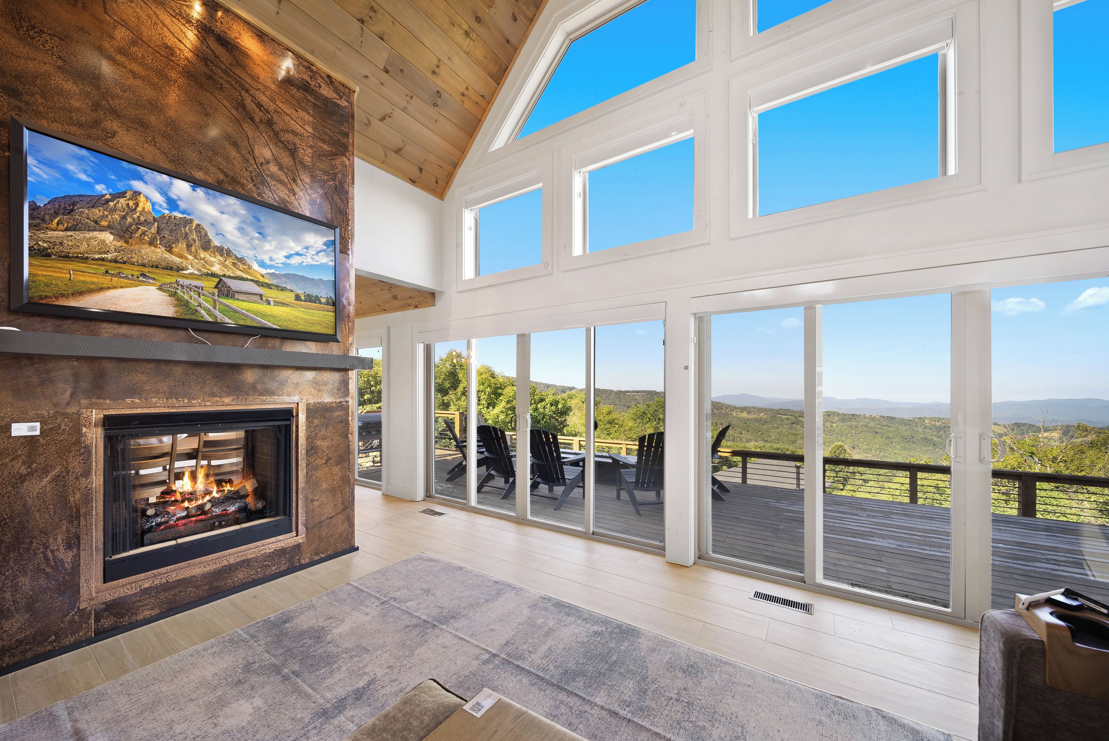 A spacious living area with a fireplace, large windows, and a deck overlooking a scenic landscape.