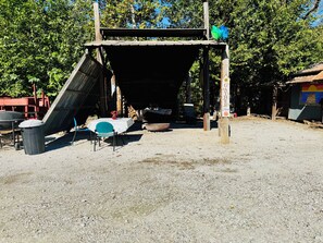 A covered outdoor area with a table and chairs, a trash bin, and a sign indicating a gathering point.