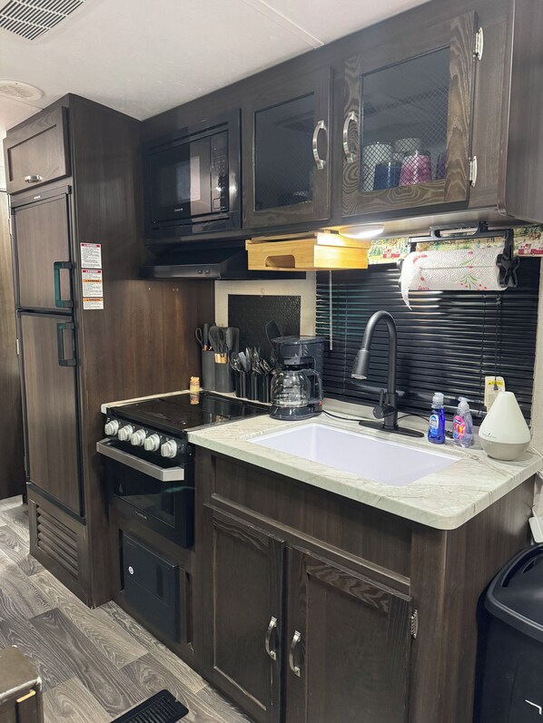 A compact kitchen with dark wood cabinets, a microwave, a stove, and a sink.