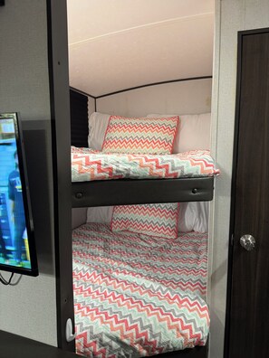 A bunk bed with a patterned bedspread and pillows, a television on the left, and a door on the right.