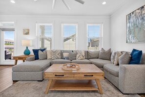 A modern living room with a sectional sofa, a coffee table, and a large window with blinds. - Coastal Paradise - Miramar Beach Escape with Pool & Golf Cart (Miramar Beach)