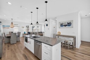 A modern kitchen with a central island, pendant lighting, and a dining area with a wooden table and chairs. - Coastal Paradise - Miramar Beach Escape with Pool & Golf Cart (Miramar Beach)