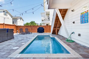 En baghave med swimmingpool, træterrasse, liggestole og et overdækket grillområde.