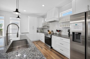 Eine moderne Küche mit weißen Schränken, Granit-Arbeitsplatten, einem Edelstahl-Kühlschrank und einem eingebauten Backofen.