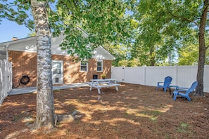 A backyard with a brick house, a white fence, a picnic table, and blue chairs. - Private Studio with Its Own Fenced Yard (Fayetteville)