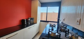 Cocina compacta con estufa a gas, armarios y ventana con vistas a un edificio.