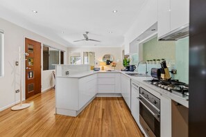 A modern kitchen with white cabinetry, a gas stove, and a ceiling fan. - Tropical 3-Bedroom Retreat Steps to the Beach (Holloways Beach)