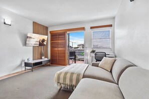 A modern bedroom with a sofa, a TV mounted on the wall, a desk, and a sliding door leading to a balcony. - Heart of the City • 1BR with Balcony & Parking (Cairns City)