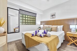 Et hotelværelse med seng, natbord, lampe og et vindue med persienner.