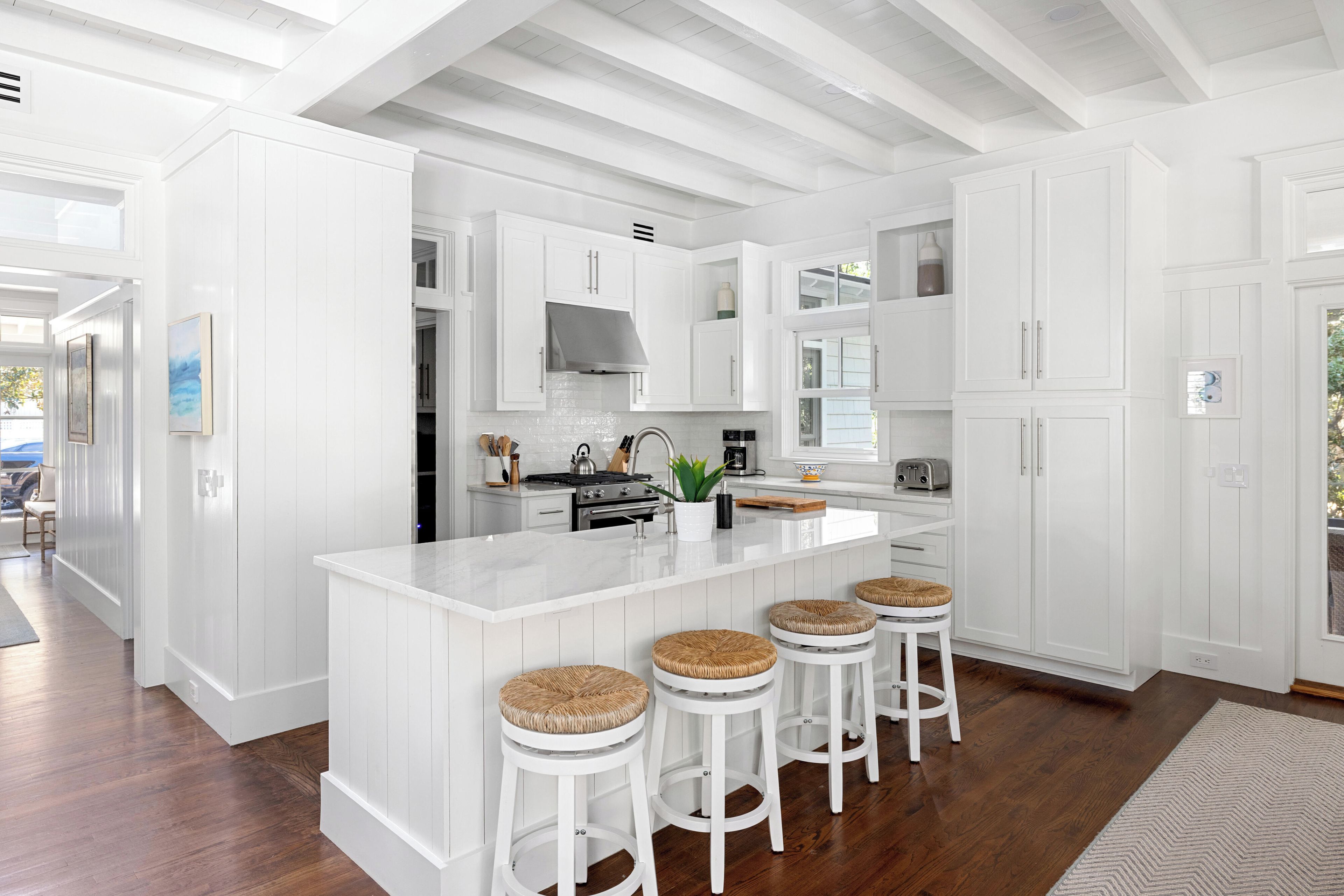 A modern kitchen with white cabinetry, a central island with stools, and a large window.