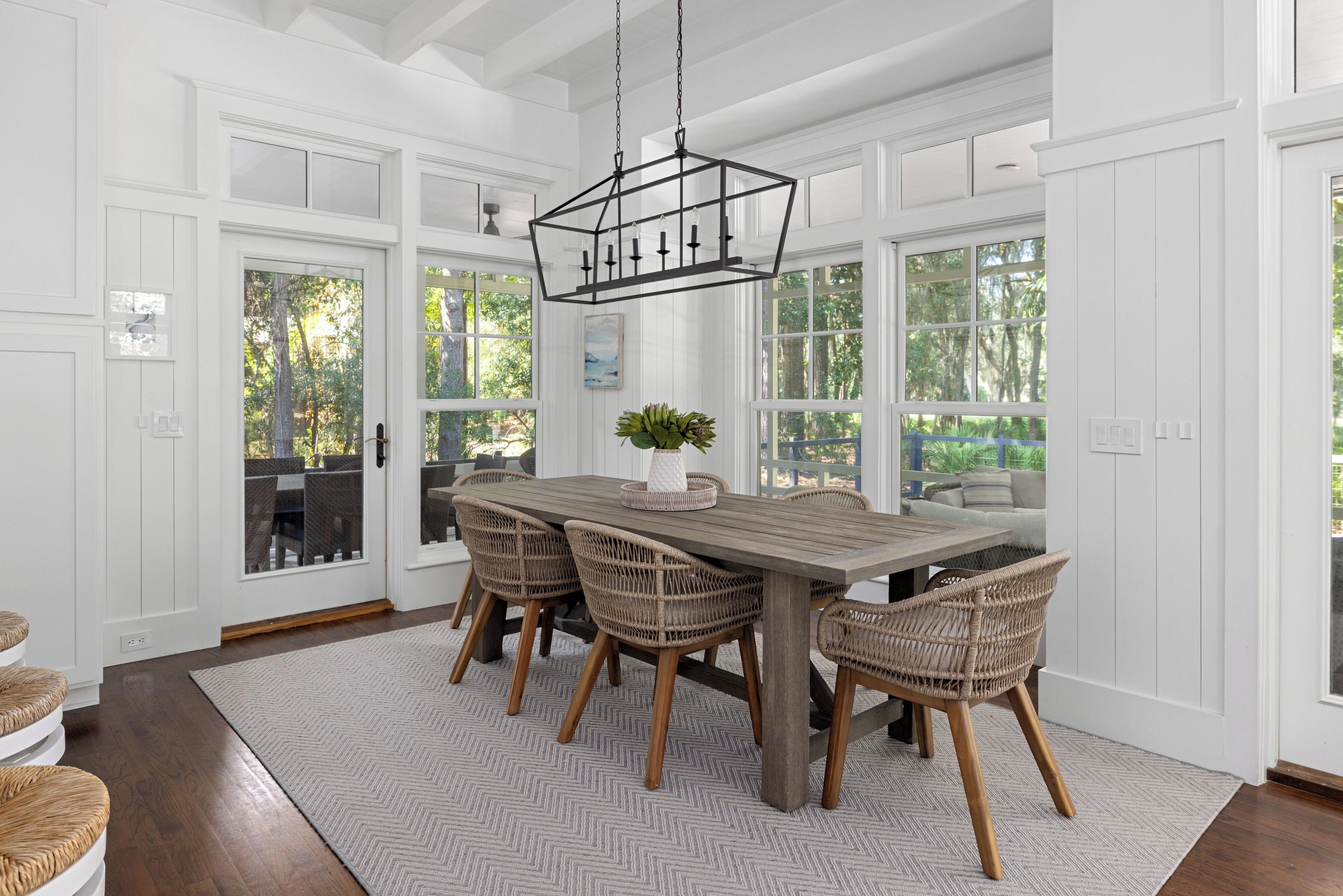 A dining area with a wooden table and wicker chairs, large windows, and a hanging light fixture.