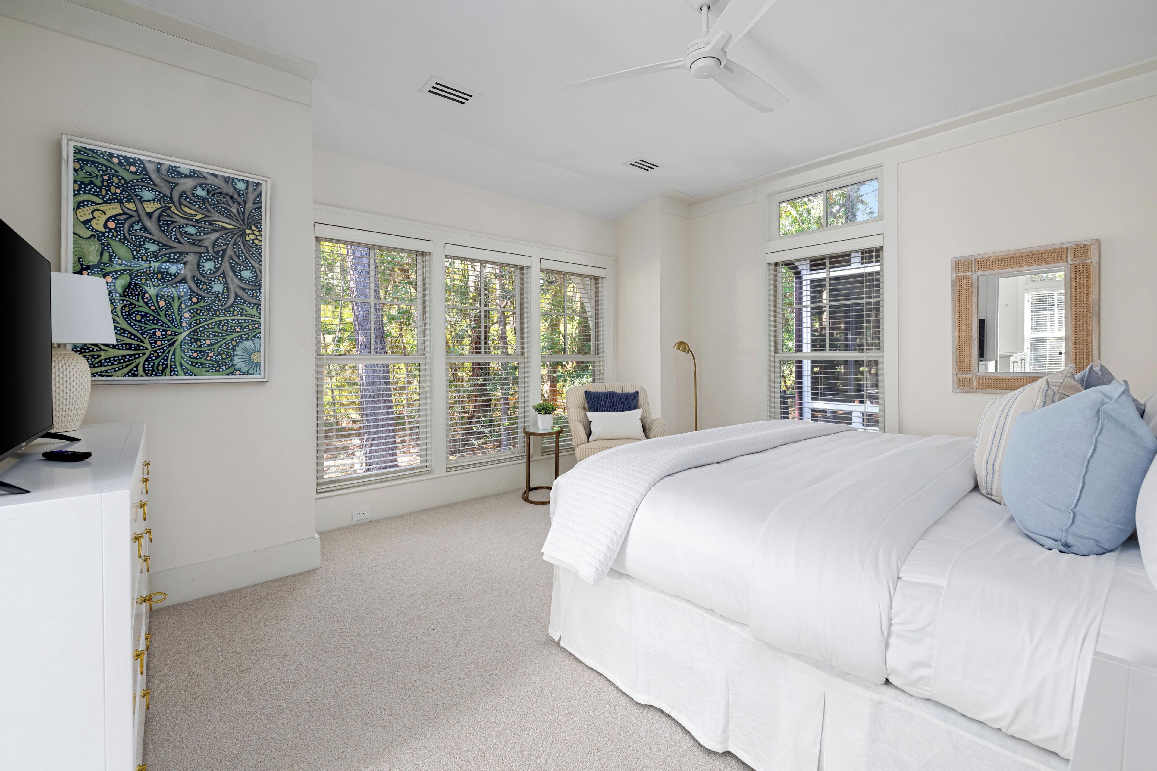 A bedroom with a large bed, a ceiling fan, and multiple windows.