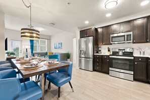 A modern kitchen with stainless steel appliances, a dining area with blue chairs, and a large window with blinds. - Stay Central, Explore More, Orlando 3BR Condo (Orlando)