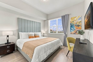 Ein modernes Schlafzimmer mit Bett, Nachttischen, Schreibtisch, Stuhl, einem Fenster mit Vorhängen und Kunstwerken an der Wand.