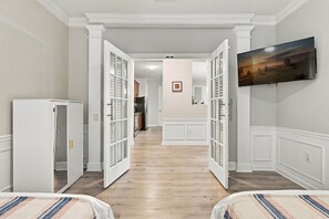 A hallway with a kitchen area in the background, a television mounted on the wall, and a door leading to another room. - Spacious 3BR in Prime Orlando Location (Orlando)