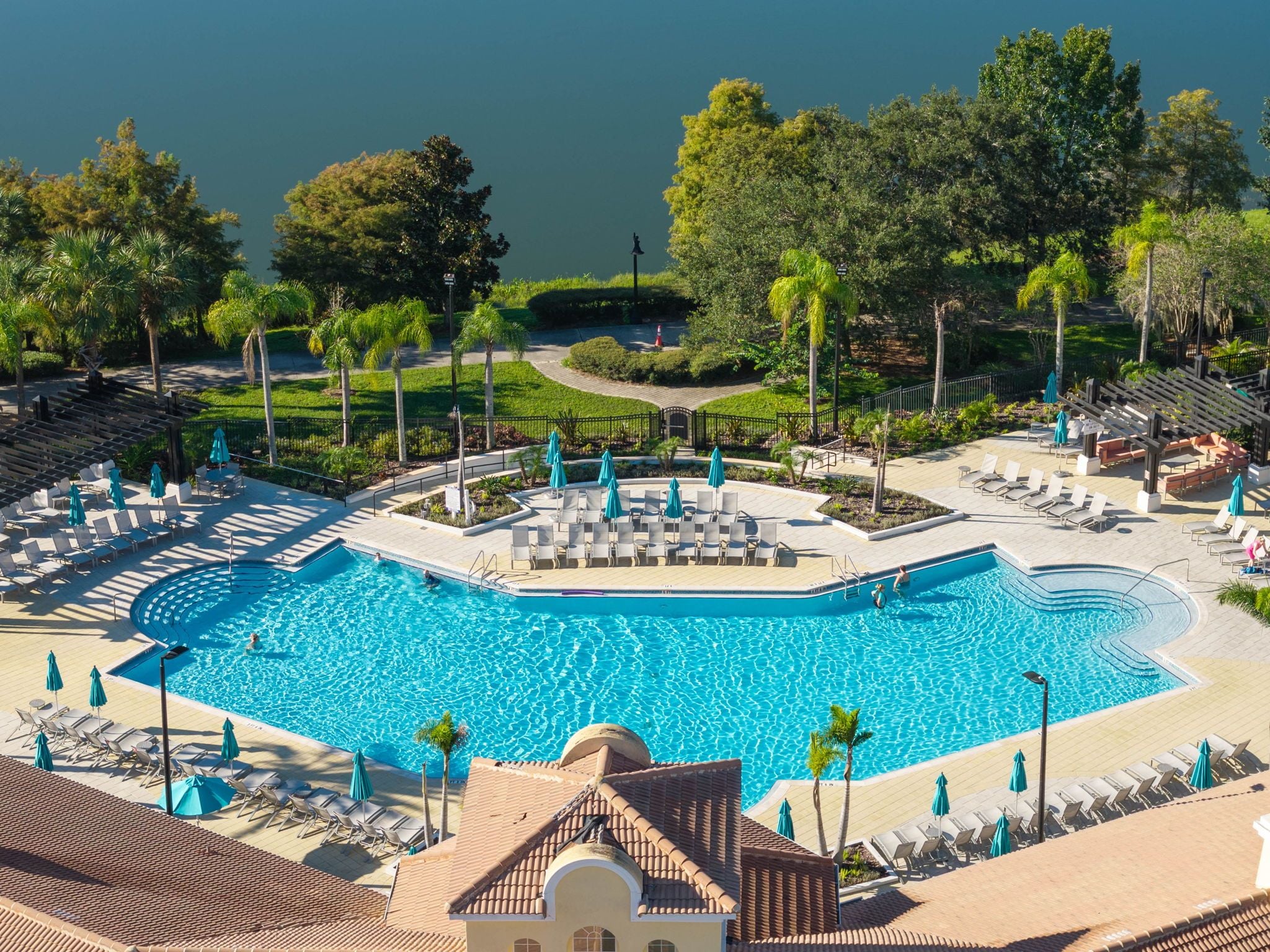 Una gran piscina con varias zonas de descanso y tumbonas, rodeada de vegetación y vistas al agua.