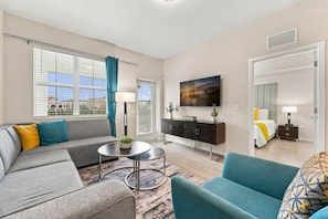 A modern living room with a sofa, armchair, coffee table, and a flat-screen TV mounted on the wall. - From Convention Days to Park Days, 3BR Condo (Orlando)