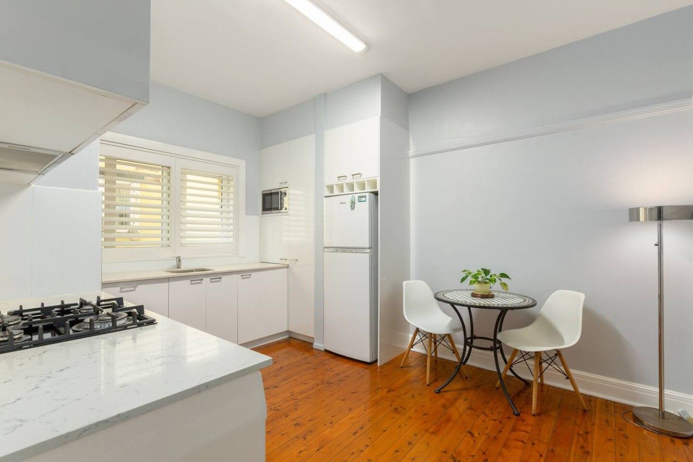 Une cuisine compacte équipée d’une cuisinière à gaz, d’un four à micro-ondes et d’un réfrigérateur, ainsi que d’une petite table à manger avec des chaises et d’un lampadaire.