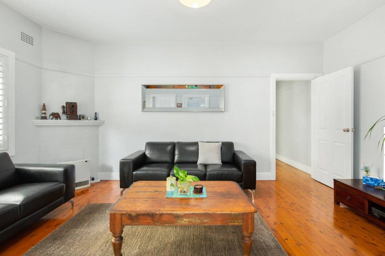 Een woonkamer met een zwarte leren bank, een houten salontafel en een open haard.