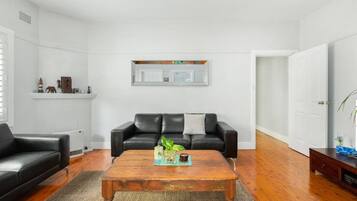 Een woonkamer met een zwarte leren bank, een houten salontafel en een open haard.