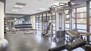 Ein Fitnessstudio mit verschiedenen Trainingsgeräten, darunter Kurzhanteln, eine Bank und Kraftgeräte.