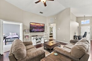 A spacious living room with a large flat-screen TV, a ceiling fan, and a view of a bedroom through an open door. - Sunny 4BR Davenport Lakes House w/ Pool & Lake Access (Davenport)
