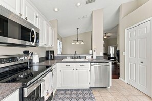 A modern kitchen with stainless steel appliances, white cabinetry, and a patterned tile backsplash. - Sunny 4BR Davenport Lakes House w/ Pool & Lake Access (Davenport)