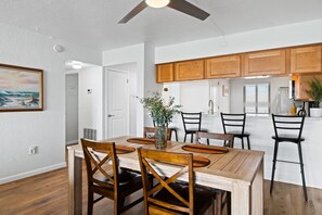 A dining area with a wooden table and chairs, a ceiling fan, and a view into the kitchen. - Seventh Heaven: 7th-Floor Ocean View Condo with Beach Access & Heated Pool in Cocoa Beach (Cocoa Beach)