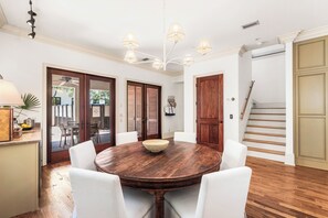 A dining area with a round wooden table, white chairs, and a chandelier. - Saltwater & Shutters Cottage - Rosemary Beach - 4 Free Bikes! (Rosemary Beach)