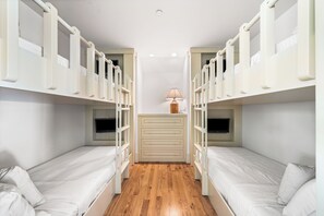 Quarto com beliches, piso de madeira, escrivaninha com gavetas e luminária.