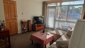 A living room with a sofa, a coffee table, a television on a stand, and a sliding glass door. - Cosy room in Inner West sanctuary near Cooks River (Dulwich Hill)