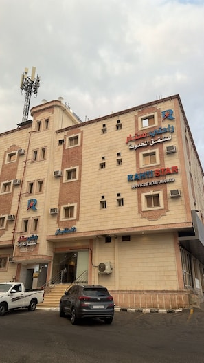 A multi-story building with a sign for 'RAHTI STAR' indicating serviced apartments. There are air conditioning units on the facade, and a parking area with vehicles. - Rahti Star 2 Serviced Apartments (taif)