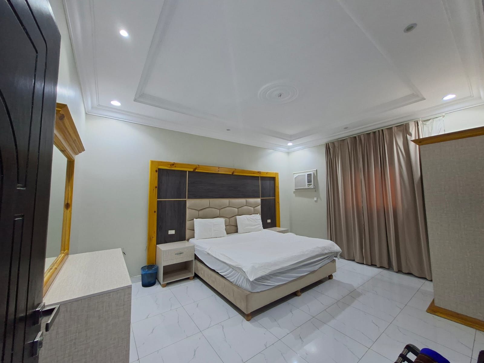 Una habitación de hotel con una cama, una mesita de noche, un armario y una ventana con cortinas.