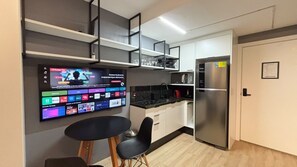 A modern kitchen with a built-in TV displaying various channels, a stainless steel refrigerator, and a dining area with a table and chairs. - Cozy studio across from Redenção Park (Porto Alegre)