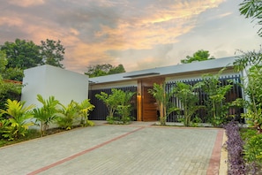 A modern house with a paved driveway, a wooden door, and a garden with various plants. - Casa Amarí: Private Pool, Rooftop Terrace and Three Ensuite Bedrooms (La Fortuna)