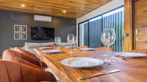 A dining area with a long wooden table set for a meal, a sofa, and a TV mounted on the wall. - Casa Amarí: Private Pool, Rooftop Terrace and Three Ensuite Bedrooms (La Fortuna)