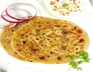 A flatbread with a golden-brown surface, accompanied by sliced red onions and a sprig of parsley. - Hotel silver stay delhi  (New Delhi)