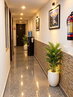 A hotel hallway with a water dispenser, potted plants, a fire extinguisher, and framed artwork on the walls. - Hotel silver stay delhi  (New Delhi)