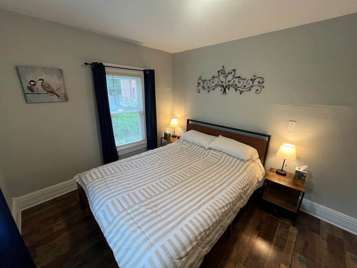 A neatly made bed with striped bedding, a window with curtains, a wall-mounted decorative piece, and bedside lamps.