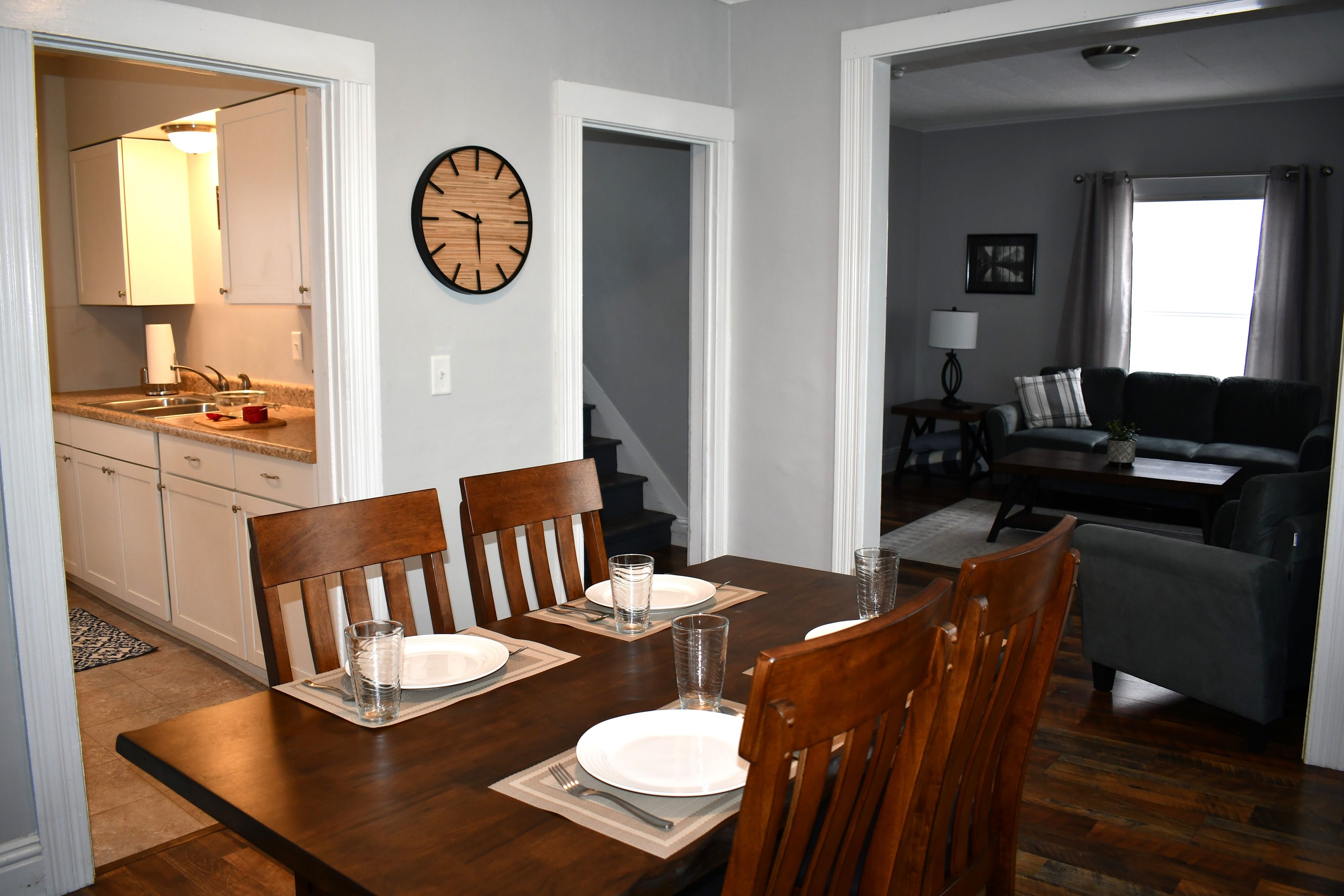 A dining area with a wooden table, four chairs, and a wall clock.