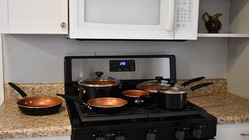 A kitchen with a gas stove, pots, a microwave, and granite countertops.