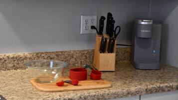 A kitchen counter with a glass bowl, red measuring cups, a wooden cutting board, a knife block, and a coffee maker.